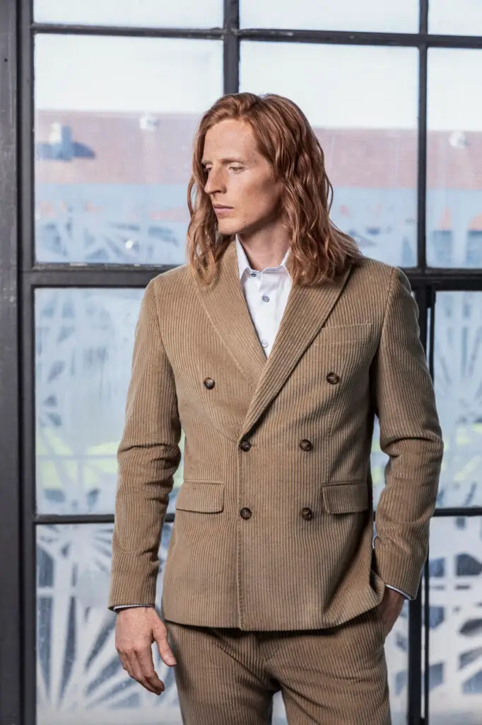 Print commercial campaign shot of a male model (name: Andreas G. Hansen) in a cortaroy suit, long red wavy hair and a a glass wall background